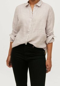 Ljusbeige linne skjorta med nedvikt krage, knäppning framtill och upprullade ärmar, kombinerad med svarta åtsittande jeans. Rens design utan mönster.