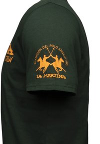 Grøn bomulds T-shirt med korte ærmer, prydet med orange tekst og to ryttere med polokøer på venstre ærme og brystet.