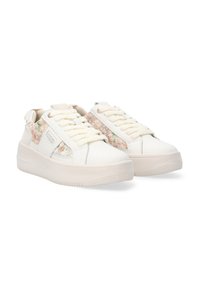 Weiße Sneakers mit floralen Stoffakzenten an den Seiten, runder Zehenpartie, flacher Sohle und dicken Schnürsenkeln. Das Material wirkt weich mit einer glatten Textur.
