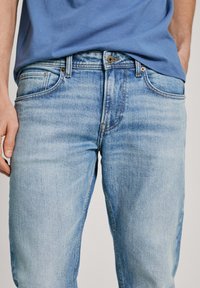 Jeans de mezclilla en un azul claro con un diseño clásico de cinco bolsillos, que incluyen un cierre de botón y un desvanecimiento sutil, mostrando una textura suave.