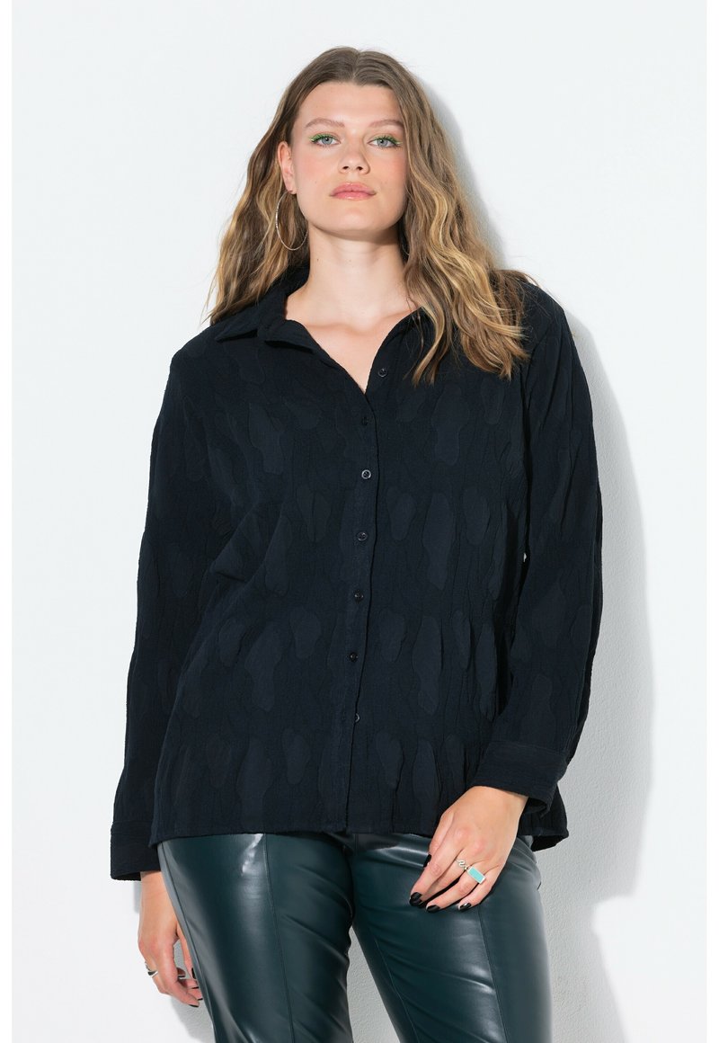 Camicia nera con bottoni a maniche lunghe e colletto, caratterizzata da un motivo testurizzato. Combinata con pantaloni in pelle verde. Design semplice senza loghi visibili.