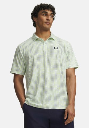 Mann trägt hellgrünes gemustertes kurzärmeliges Poloshirt mit Kragen und dunkle Hose, steht mit den Händen in den Taschen und schaut zur Seite.