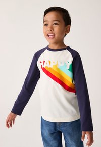 Majica z dolgimi rokavi, bela osnovna barva z mornarsko modrimi rokavi, mavrični vzorec in beseda "HAPPY" izrezana iz tkanine. Prijeten, sproščen kroj.