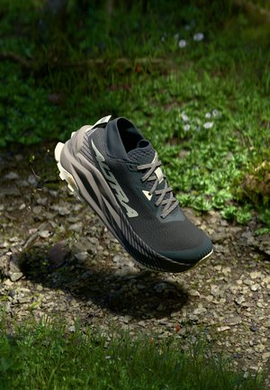 Black athletic shoe with textured upper and beige accents, featuring a streamlined design, prominent laces, and a multi-directional traction sole.