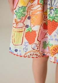 Lähikuva värikkäästä kankaasta, jossa on kuvituksia mansikoista, juomista, kukista ja sana "STRAWBERRIES" lapsen mekossa.