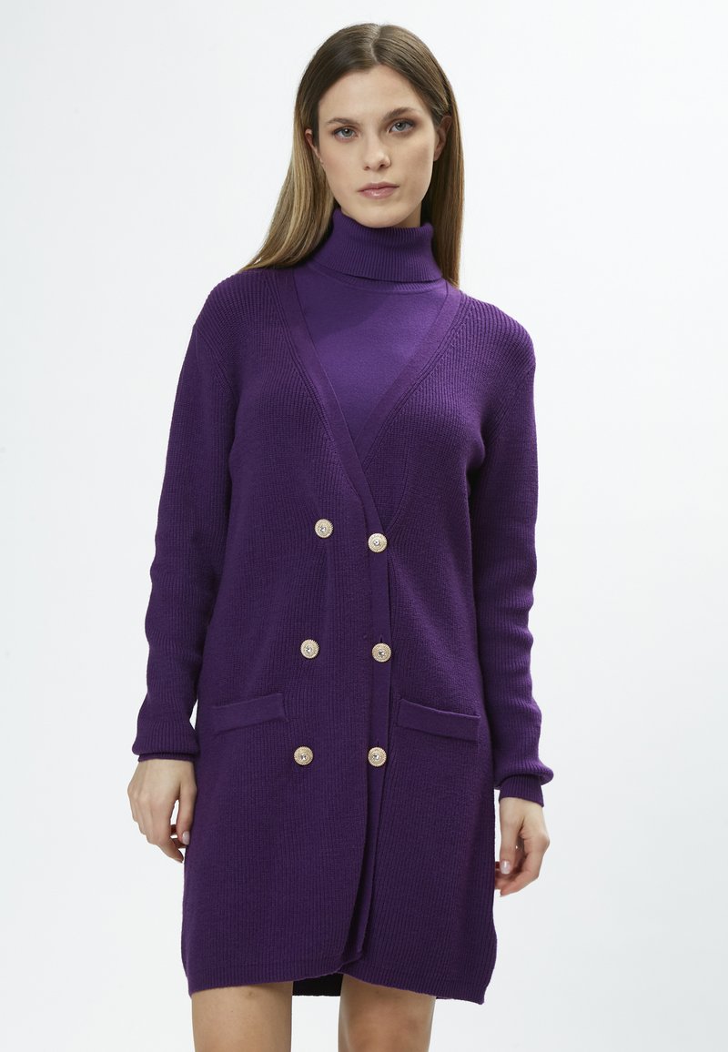 Cardigan en tricot violet avec de longues manches, col en V, deux poches avant et six grands boutons décoratifs sur le devant.