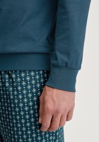 Donkerblauw hemd met lange mouwen en geribbelde manchetten, gecombineerd met gestreepte broek met een geometrisch ontwerp in groene en blauwe tinten.