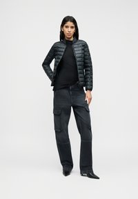 Μαύρο μπουφάν puffer με σχεδιασμό καπιτονέ, σε συνδυασμό με εφαρμοστό μαύρο τοπ και φαρδιά τζιν cargo. Μαύρα παπούτσια με ψηλό τακούνι.