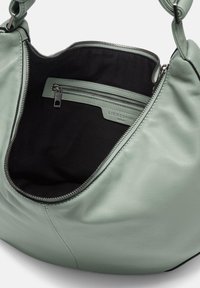 Bolso de mano de cuero verde menta con un amplio interior negro, bolsillo con cremallera y cierre de cremallera metálico. Textura suave con forma redondeada.