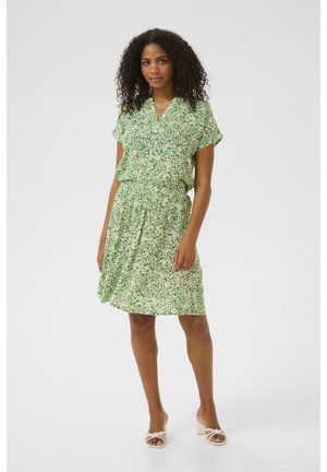 Green floral dress with a v-neck, short sleeves, and gathered waist. Fabric features small, multicolored flower patterns and a flowing design.