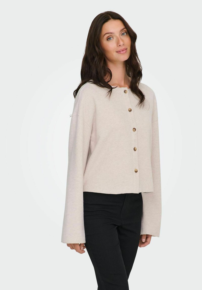 Jasno beżowy krótki kardigan z długimi rękawami i okrągłym dekoltem, z drewnianymi zapięciami z przodu. Miękka tekstura.