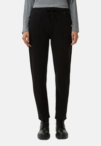 Zwarte joggingsbroek met een aantrekkoord in de taille, voorzien van zijzakken en gestikte details voor textuur. G gedragen met zwarte veterschoenen.