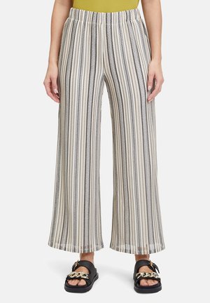 Bredde ben bukser i creme med sorte lodrette striber. Elastisk talje. Stoffet har en subtil struktur. Båret med sorte sandaler med en guldkæde.