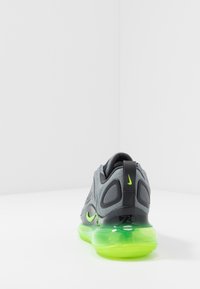 Grå idrottssko med svarta accenter, meshupp överdel och en genomskinlig grön sula. Har en vadderad krage och logotyp på hälen.