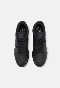 Czarne buty sportowe z gładką syntetyczną cholewką i teksturowanymi akcentami, wyposażone w miękki kołnierz, sznurowadła oraz logo na języku.