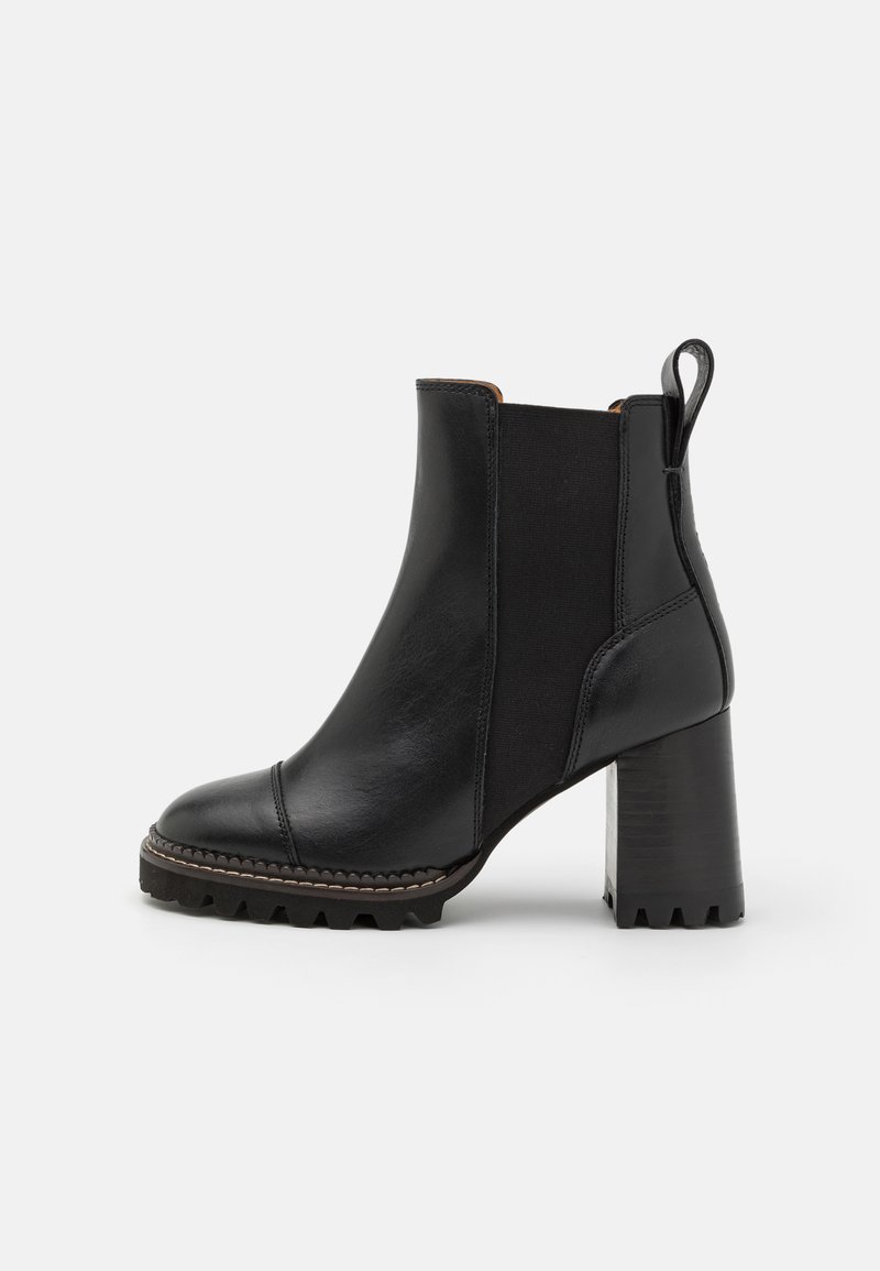 Bottine en cuir noir avec un talon épais, panneaux latéraux élastiques et une semelle texturée. Comprend un bout capuchon cousu et une languette de tirage.