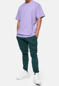 Purple cotton t-shirt with short sleeves paired with dark green sweatpants. White sneakers complete the casual outfit.