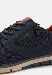 Baskets en maille navy avec accents en cuir marron, dotées de lacets, d'un corps texturé et d'un patch logo noir. Semelle en caoutchouc avec rainures pour l'adhérence.