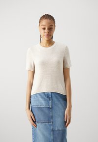 Beige, gestrickter Kurzarm-Pullover mit Rundhalsausschnitt. Kombiniert mit einem Jeansrock mit Patchwork-Details und einem rohen Saum.