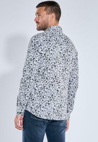 Weißes Hemd mit grünem Blumenmuster, langen Ärmeln, Knopfmanschetten und spitzem Kragen, getragen mit marineblauen Jeans.