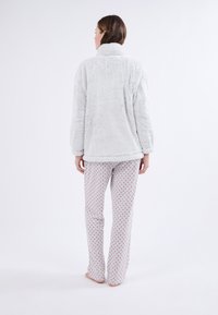 Chaqueta esponjosa de color gris claro con un cuello alto, combinada con pantalones de pijama blancos con puntos rojos. Ajuste suave y relajado.