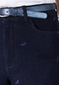 Donkerdenim jeans met een subtiel patroon van hoge hakken. Beschikt over een glanzende blauwe riem met een gestructureerd oppervlak en een zilveren gesp.