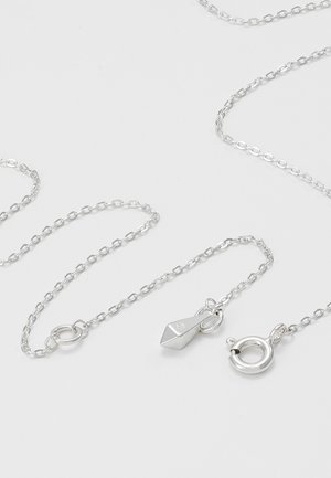 Delicate zilveren ketting met ovale schakels, voorzien van een veerring sluiting en een kleine geometrische zilveren hanger op een lichte achtergrond.