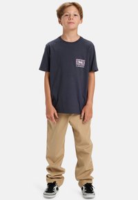 Navy short-sleeve t-shirt with a front graphic pocket design. Paired with khaki pants and black sneakers with white accents.