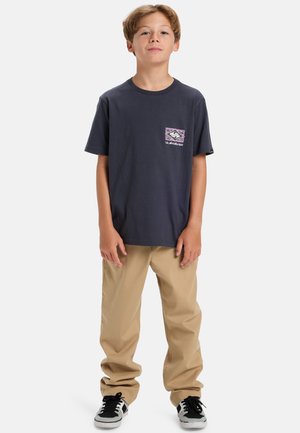 Marineblå t-skjorte med kort erme og grafisk lomme-design foran. Kombinert med khaki-bukser og svarte joggesko med hvite detaljer.