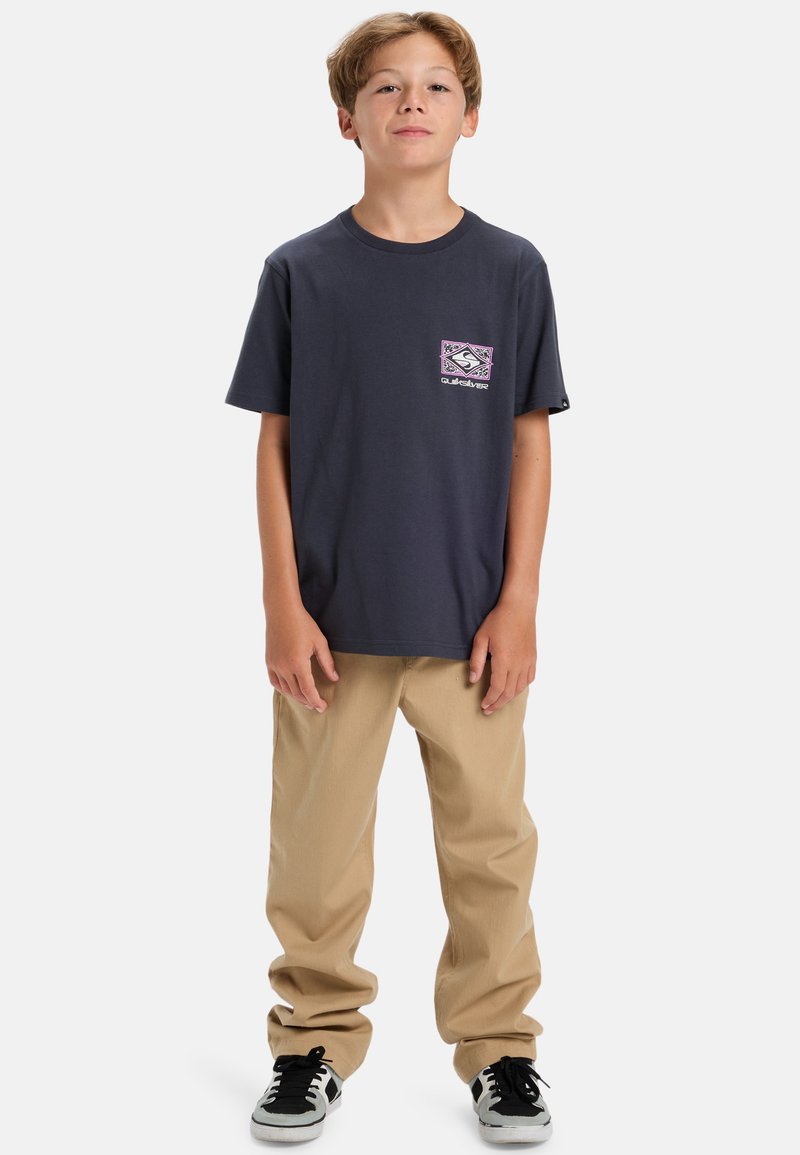 Navy short-sleeve t-shirt with a front graphic pocket design. Paired with khaki pants and black sneakers with white accents.