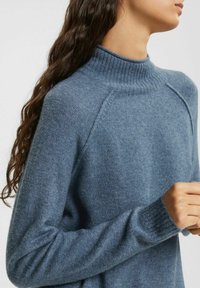 Ljusblå, mjukstickad tröja med hög ribbad krage, raglanärmar och ribbade muddar, med en slät textur och avslappnad design.