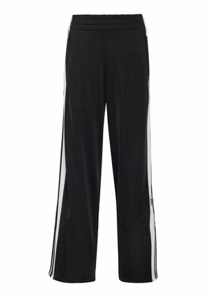 Zwarte losse trainingsbroek met elastische tailleband, witte en zwarte strepen aan de zijkant en een klein logo bij de linkerknie.