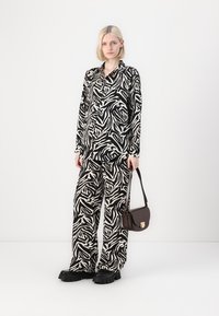Svartvit zebra-mönstrad skjorta och byxset med vida ben, parat med klumpiga svarta skor och en liten brun axelremsväska.