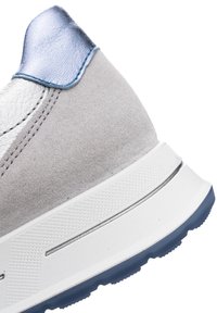 Tacón de zapatilla de ante gris con suela blanca y azul y detalle metálico azul en el collarín del tobillo sobre fondo blanco.