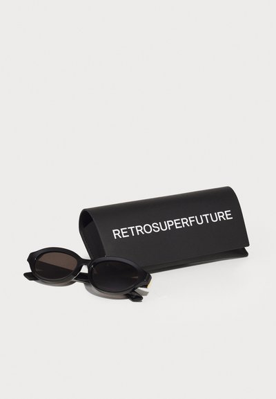 Des lunettes de soleil noires de forme ovale avec des verres foncés, une finition mate et des accents dorés. Accompagnées d'un étui noir avec un texte blanc.