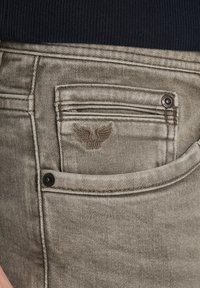 Jeans de denim gris de corte ajustado con un acabado texturizado, que presentan un pequeño bolsillo y un logotipo de ala bordado sobre el bolsillo para monedas.