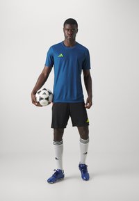Tricou sportiv albastru cu accente verzi, pantaloni scurți negri, șosete albe cu dungi negre, ghete de fotbal albastre și o minge de fotbal alb-negru.