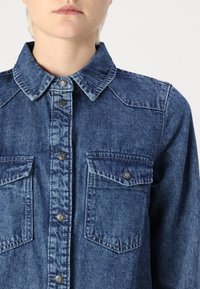 Jeansskjorta i mörkblått med klassisk krage, framknäppning och två bröstfickor med knappstängningar. Strukturerad tyg.