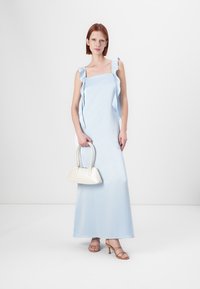 Světle modré maxi šaty s volánovými ramínky, hladká textura, kombinované s bílou kabelkou a sandály na vysokém podpatku. Jednoduchý a elegantní design.