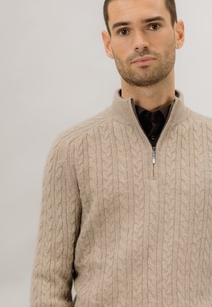 Beige kabelstrikket genser med høy krage og kvart glidelås. Myk tekstur; subtile detaljer i strikkemønsteret.