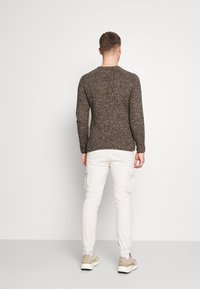 Brauner und mehrfarbiger gestrickter Pullover mit langen Ärmeln, gerippten Bündchen und Saum. Kombiniert mit weißen Cargohosen und hellen Sneakern.