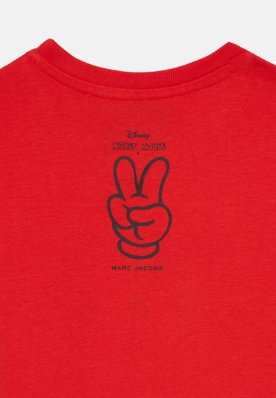 Punane puuvillane T-särk ümmarguse kaelusega. Seljal on must graafika, kus on kujutatud Mickey Mouse'i rahu märk ja tekst "MARC JACOBS".