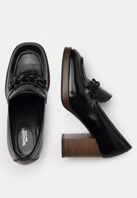 Mocasines de charol negro con un tacón grueso imitación madera y un detalle de cadena en la parte frontal. Textura suave y diseño elegante.