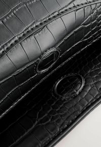 Intérieur d'un sac à main en cuir noir avec un motif crocodile. Présente un matériel circulaire et des détails cousus, mettant en valeur des surfaces lisses et texturées.