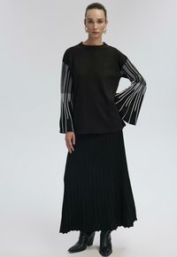 Black long-sleeve top with white vertical stripes, paired with a pleated black skirt. The outfit features fitted cuffs and black ankle boots.