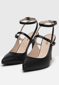 Czarne skórzane buty na wysokim obcasie z wąskimi paskami przy kostce, centralnym paskiem oraz szpiczastymi noskami. Teksturowane wykończenie i smukła, elegancka sylwetka.