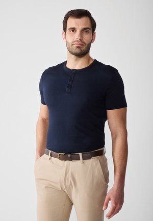 Navy blue short-sleeve henley shirt with three buttons, paired with beige trousers and a brown belt, featuring a smooth texture and fitted design.