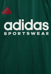 Camisa de deporte verde con el distintivo texto en blanco "adidas" y "SPORTSWEAR" debajo. Logo rojo de adidas en la esquina superior izquierda. Textura de rayas verticales.
