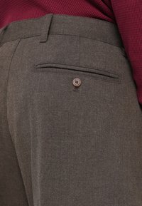 Pantaloni de culoare maro închis cu un model texturat de herringbone, având un buzunar pe spate cu un singur detaliu de nasture maro.