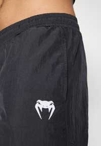 Sorte shorts lavet af letvægtsstof, med en elastisk talje og et hvidt slangerlogo på siden. Tekstureret mat finish.